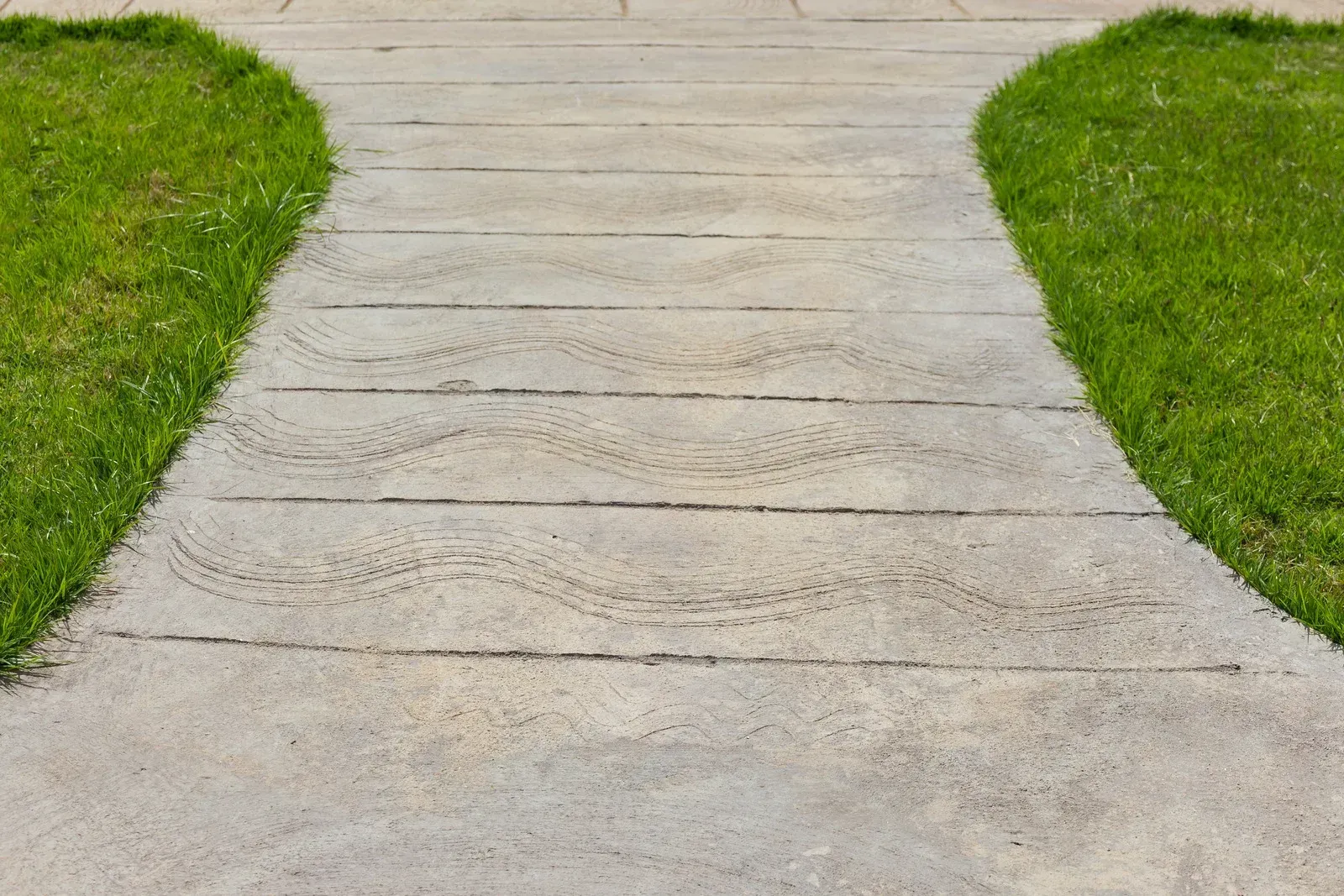 Concrete path with tire tracks curving between patches of green grass.