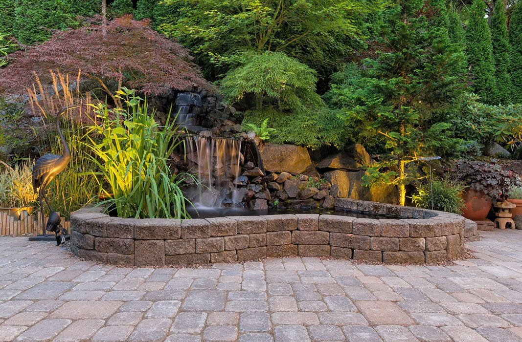 Landscaped front yard with red mulch, stone borders, and various green plants. Concrete walkway.