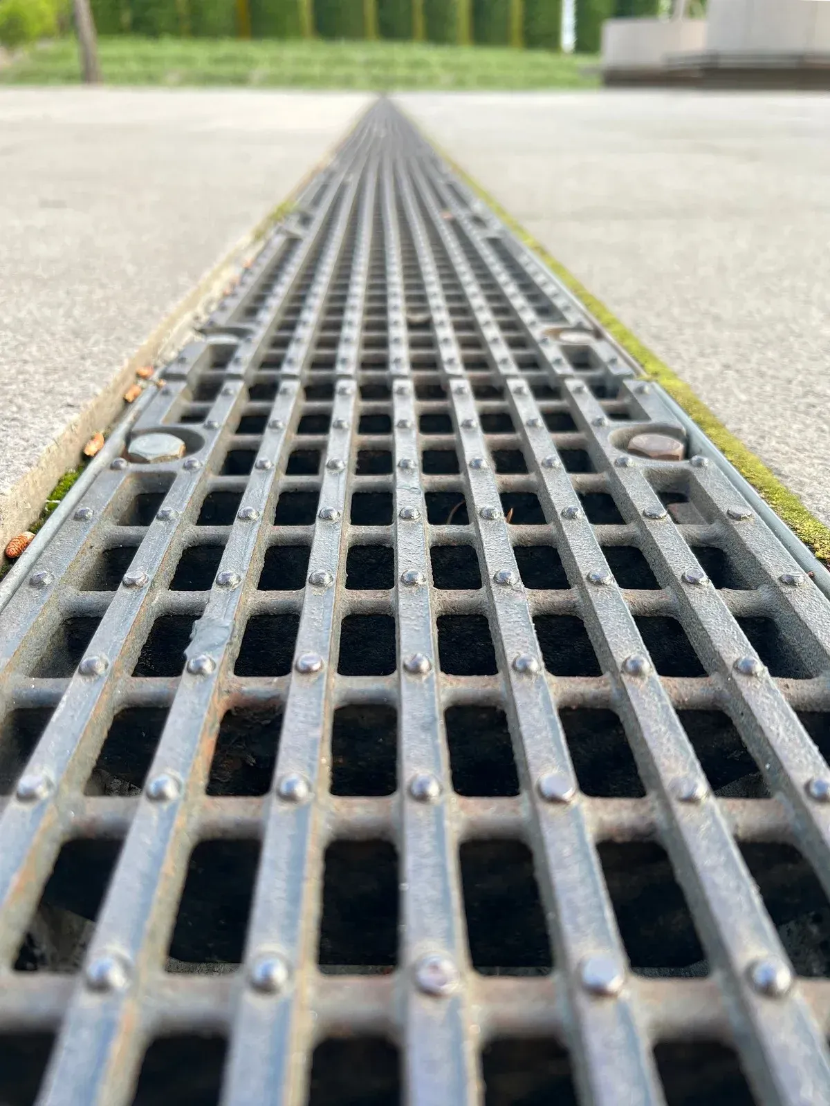 Metal grating in a sidewalk, leading into the distance.