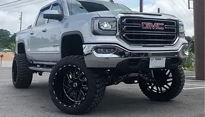 A silver gmc truck with black wheels and tires is parked in a parking lot.