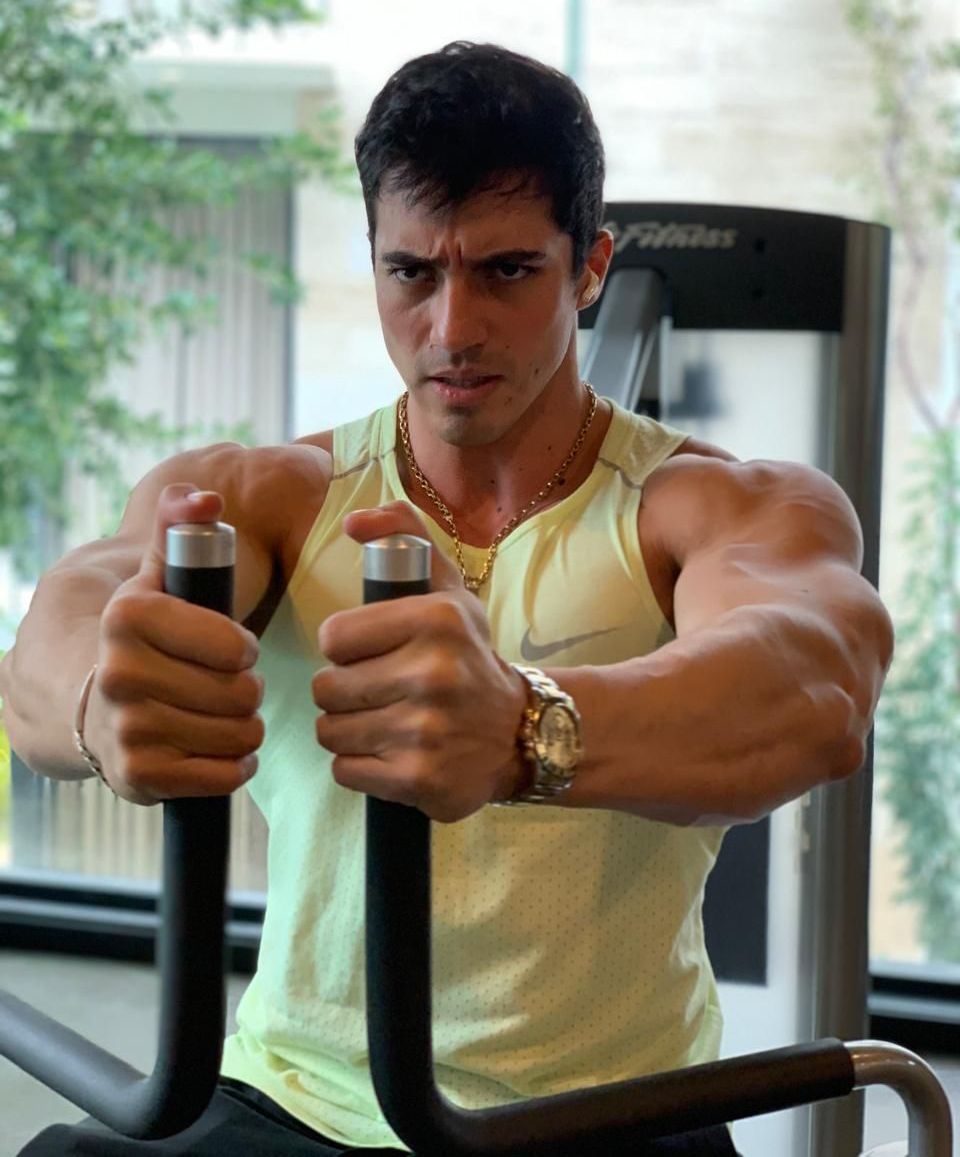 A man in a yellow tank top is using a machine in a gym.