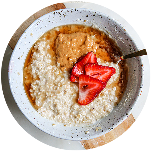 A bowl of oatmeal with strawberries and peanut butter on top.