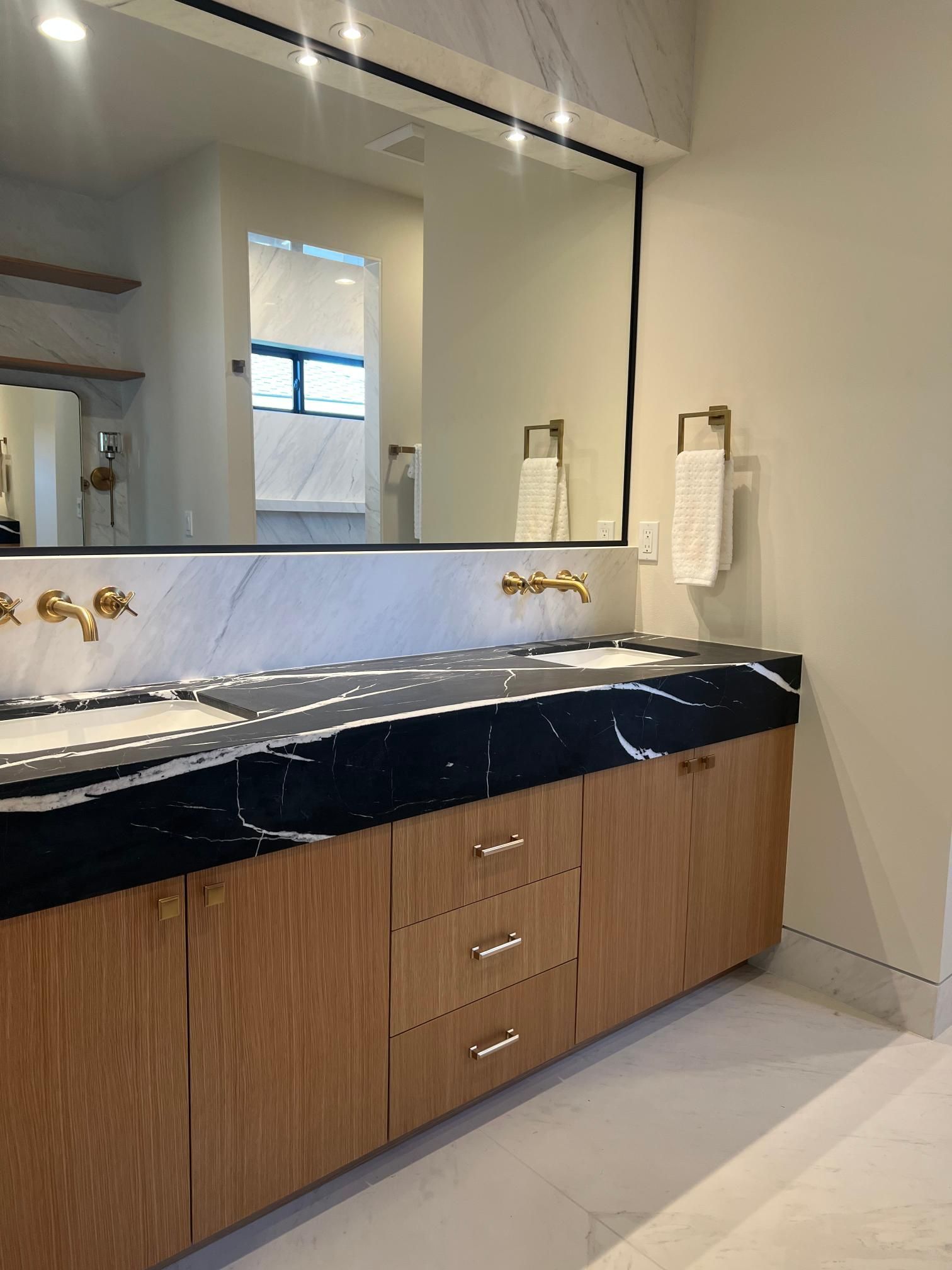 Modern bathroom with a black marble countertop, wooden cabinets, and a large mirror.