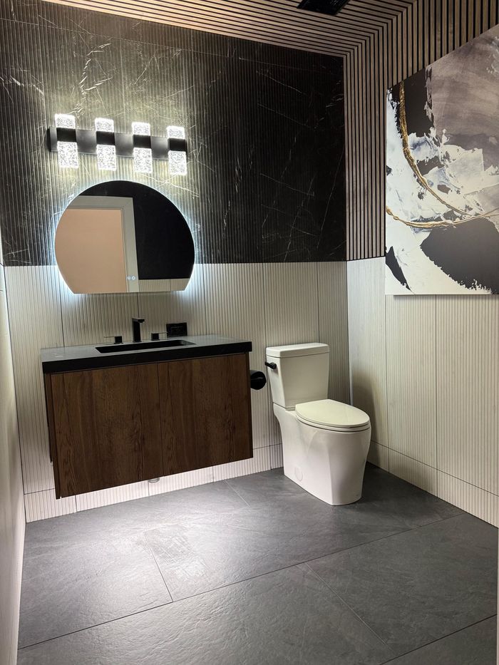 Modern bathroom with floating wood vanity, round mirror, and textured black wall.
