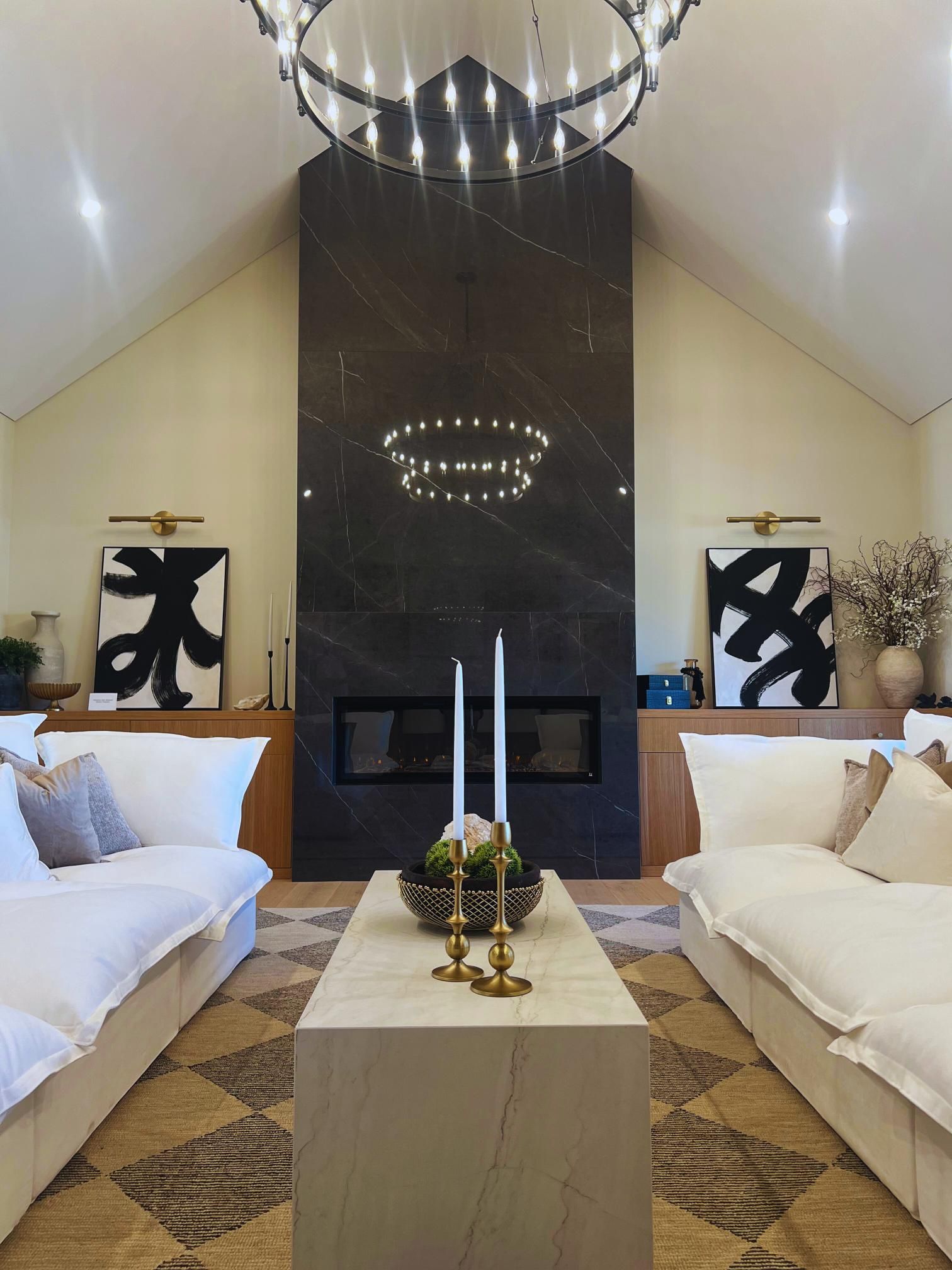 Living room with marble fireplace, white sofas, and modern chandelier.