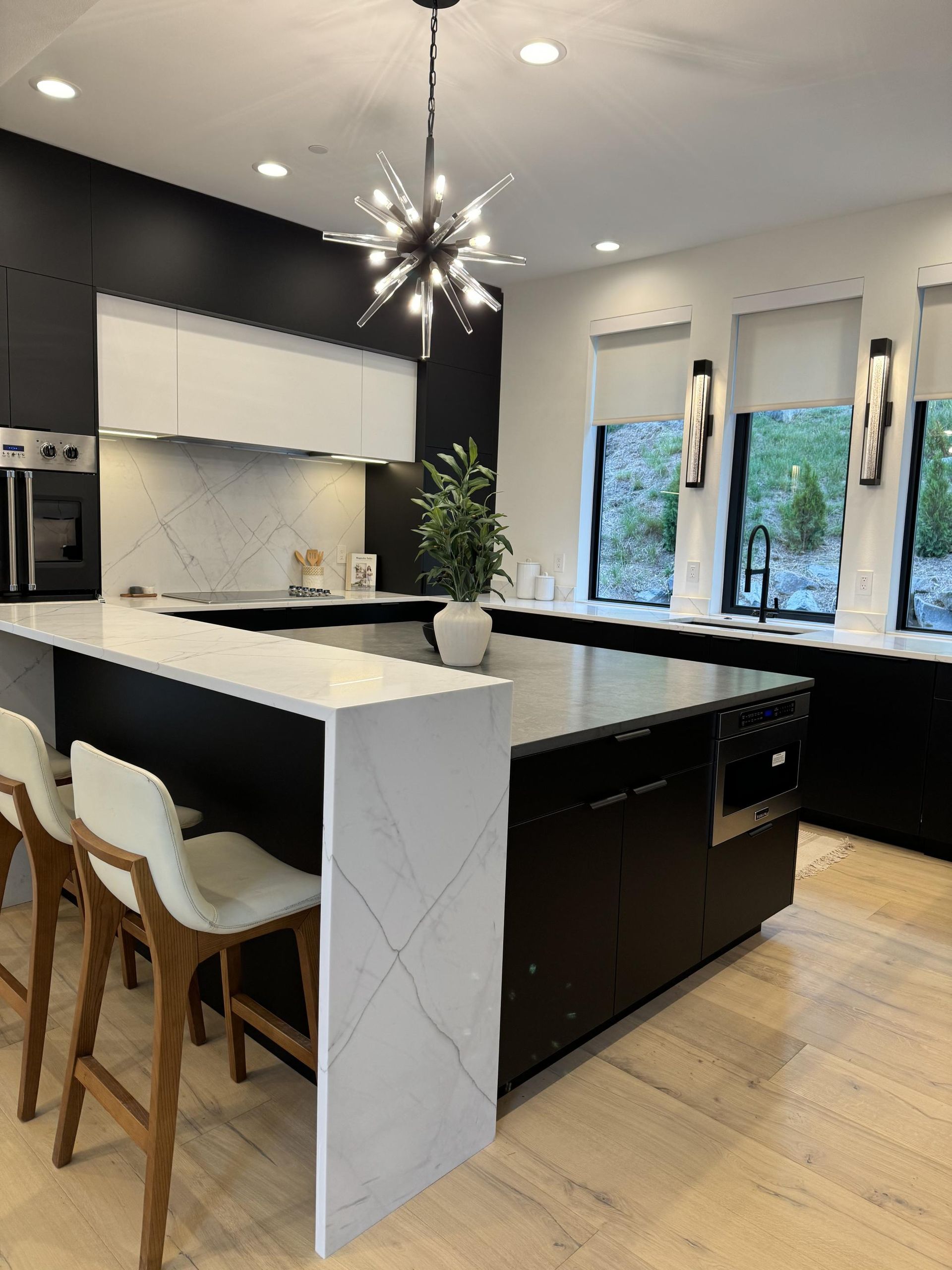 Modern kitchen with black island, white counters, and gold pendant light.