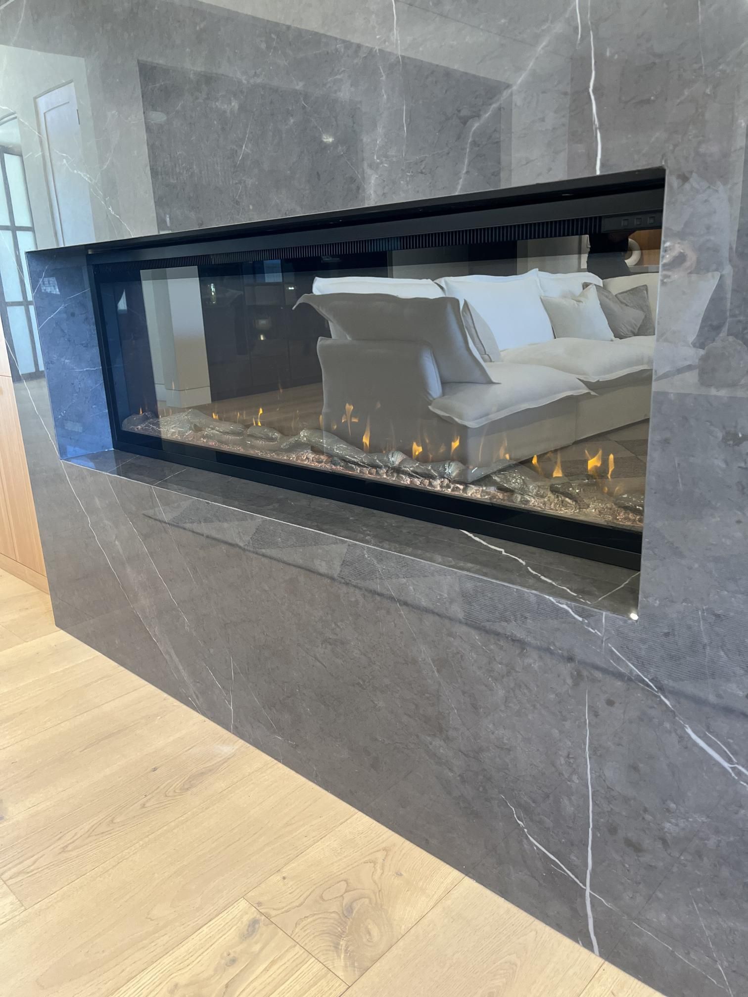 A modern fireplace built into a marble wall, with a glimpse of a white couch.