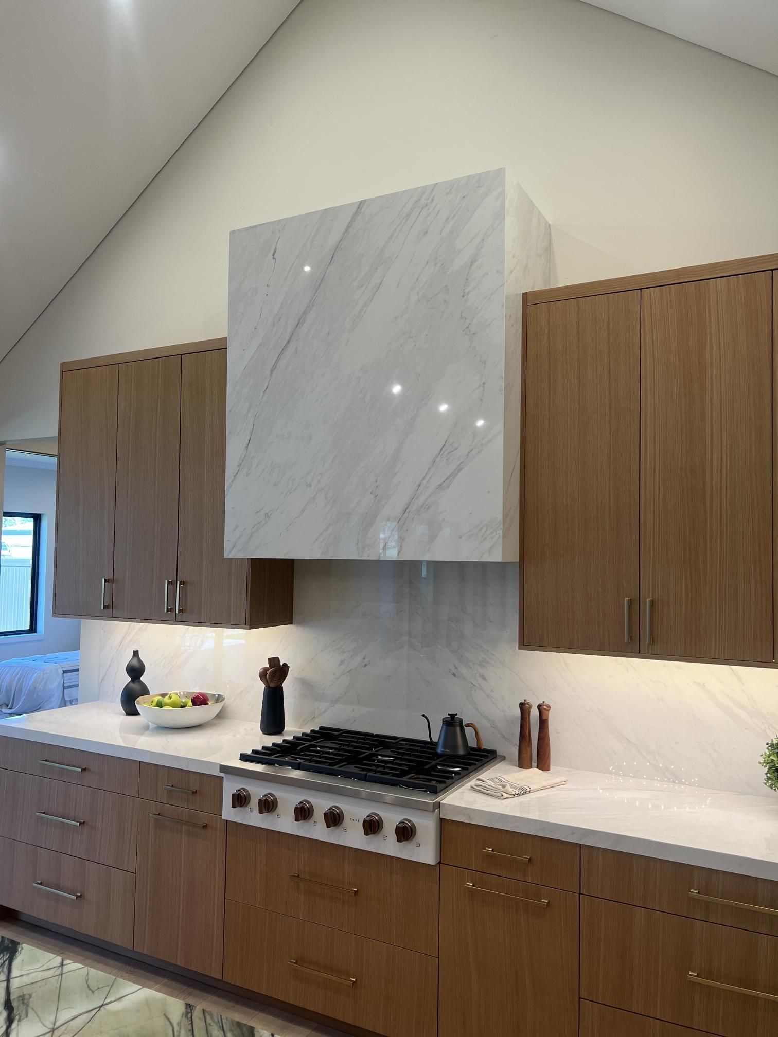 Modern kitchen with white marble range hood, wood cabinets, and stainless steel stove.