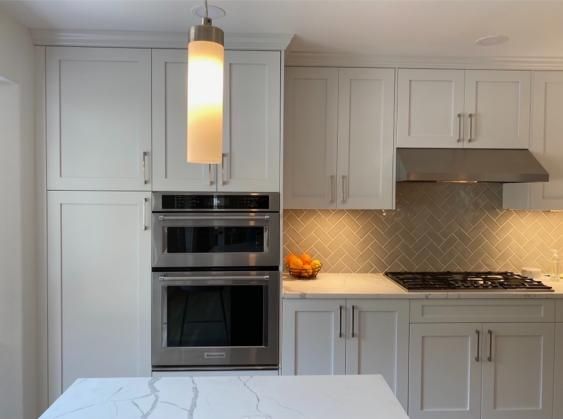 White kitchen with oven, cabinets, pendant light, and countertop.