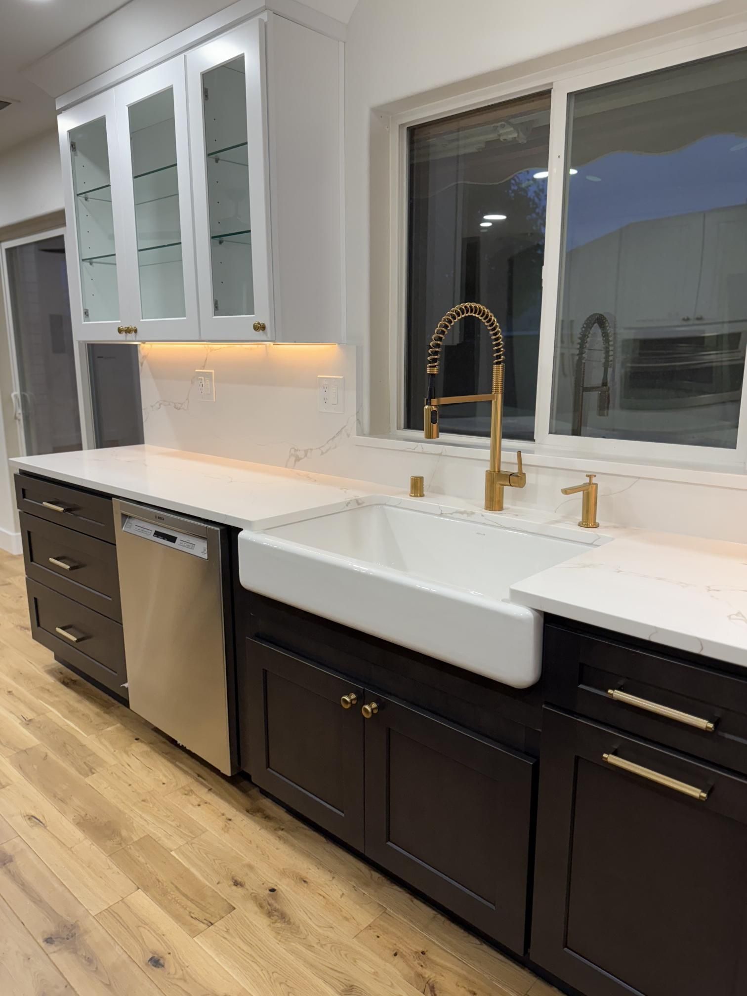 Modern kitchen with dark cabinets, white countertop, gold faucet, and farmhouse sink.