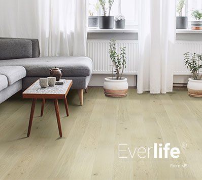 Living room with light wood floor, gray couch, coffee table, and plants.