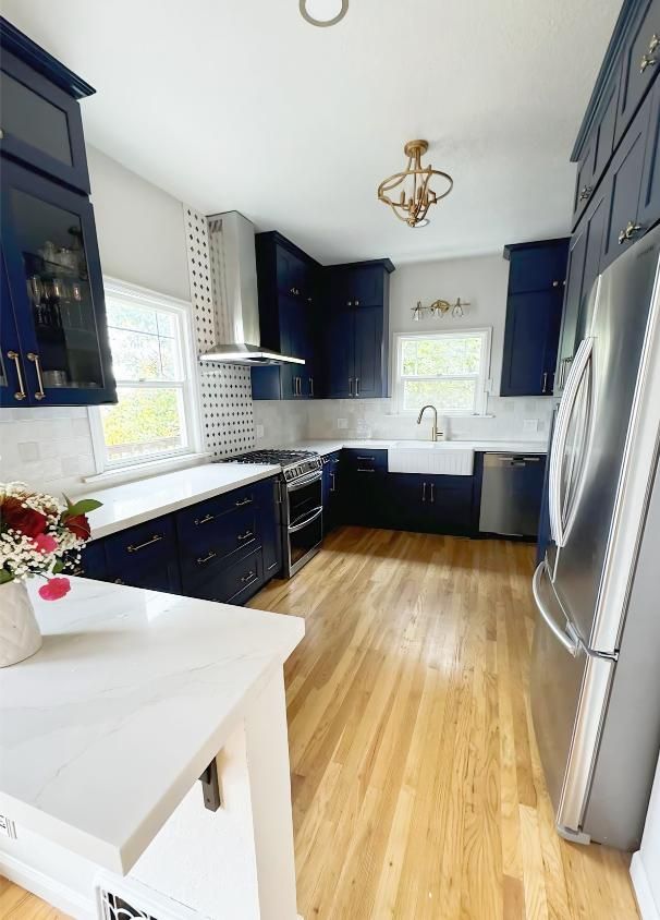 Kitchen with navy blue cabinets, stainless steel appliances, white countertops, and hardwood floors.