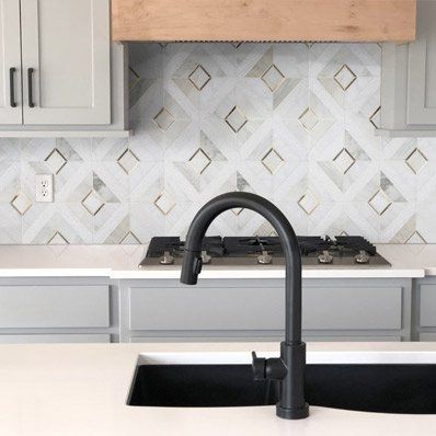 Modern kitchen with gray cabinets, white countertops, and black faucet. Diamond patterned backsplash.