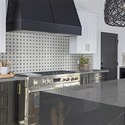 Modern kitchen with stainless steel range, black hood, and patterned tile backsplash.