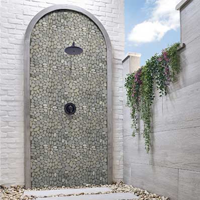 Outdoor shower with pebbled wall, black fixtures, and trailing plants.