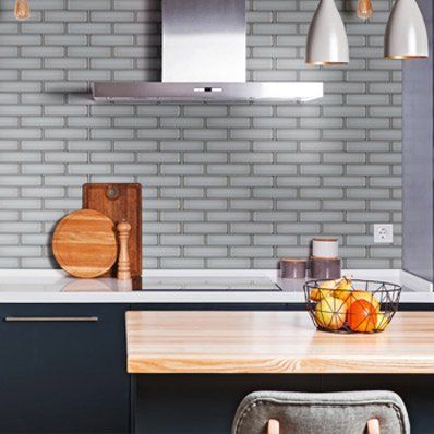 Kitchen with blue brick backsplash, stainless steel hood, wooden countertop, fruit basket, and dark blue cabinets.