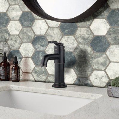 Black faucet on a white countertop with a hexagonal tile wall and a mirror.
