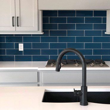 Kitchen with blue tile backsplash, white countertops, gray cabinets, and black faucet.