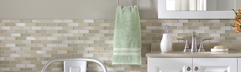 Bathroom with green towel, sink, white cabinet, and tile backsplash.