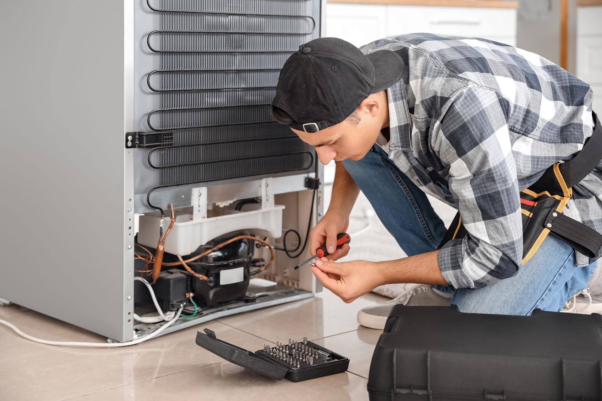 A man is fixing a refrigerator in a kitchen.