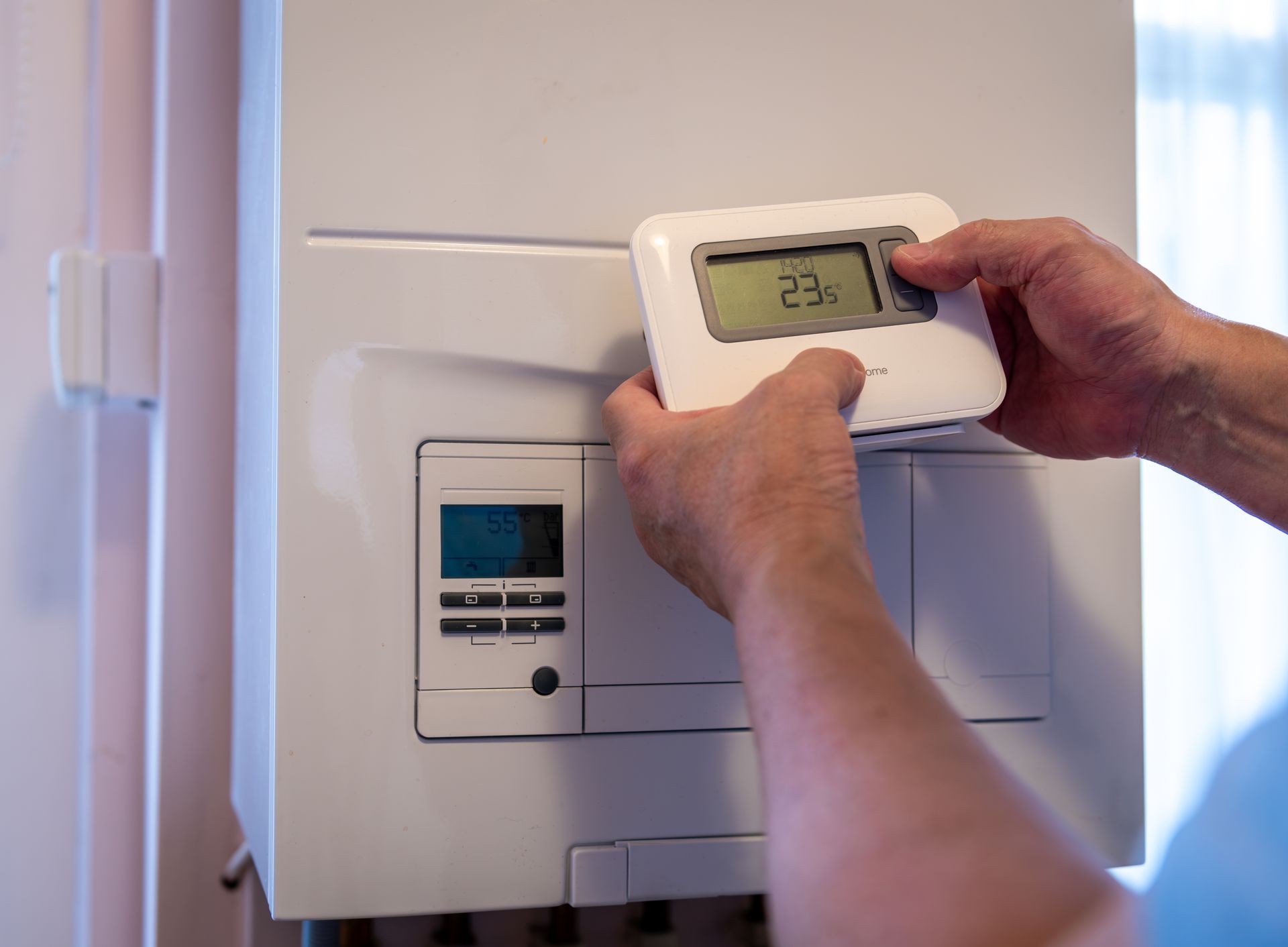 A person is adjusting a thermostat on a boiler.