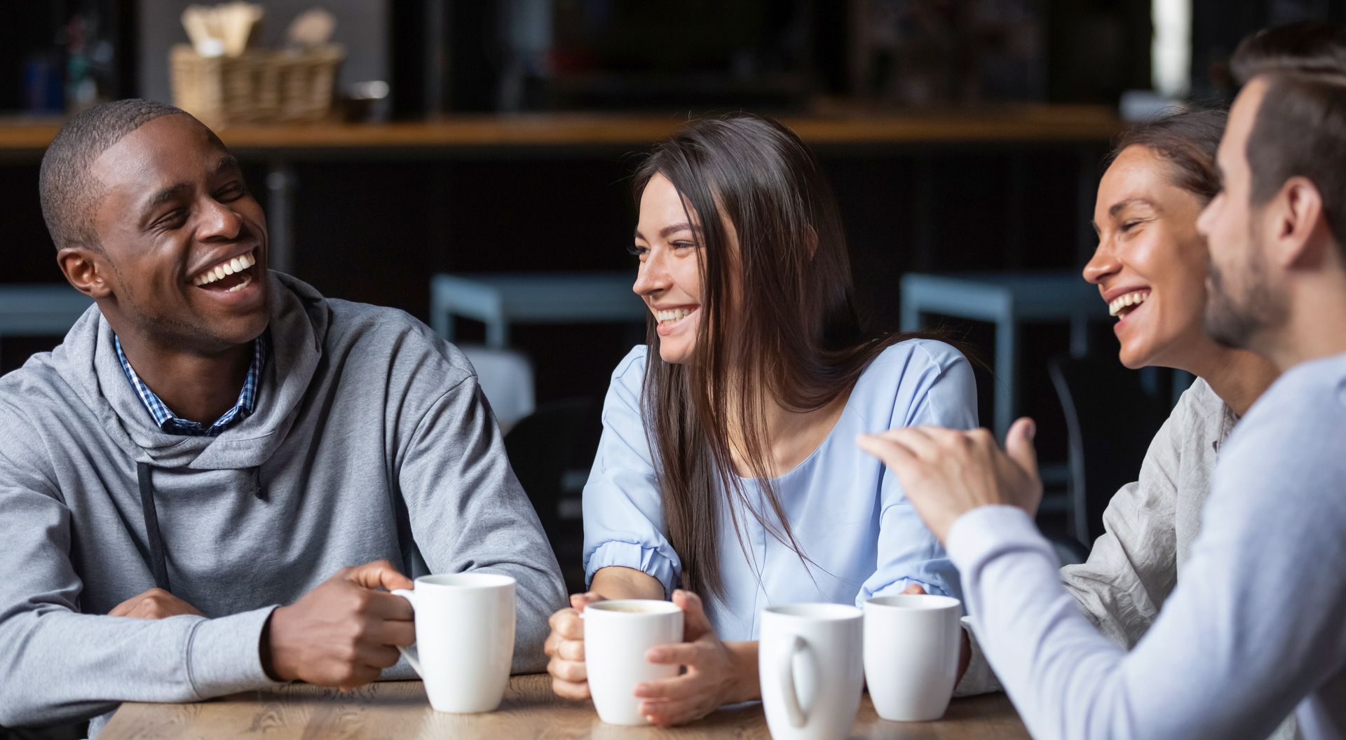 Four people laughing and drinking coffee at a cafe table.