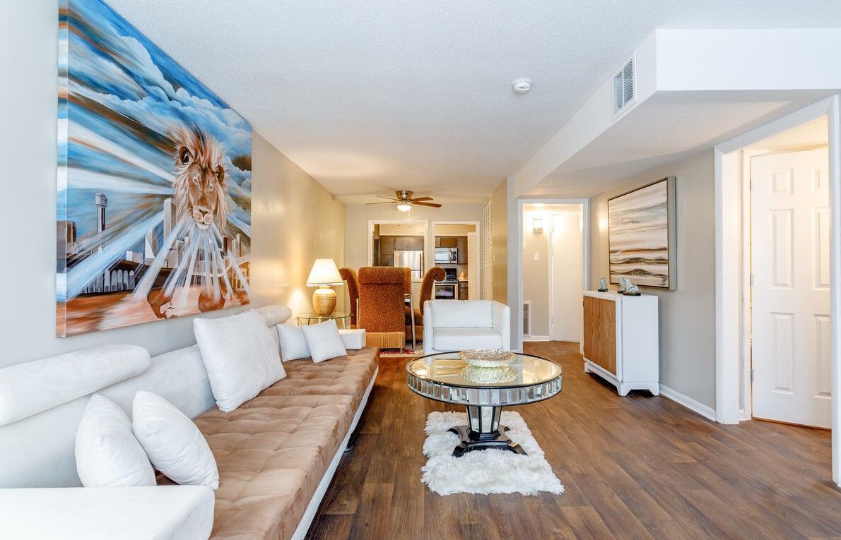 Living room with brown and white furniture, art, and a round mirrored coffee table on a fluffy rug.