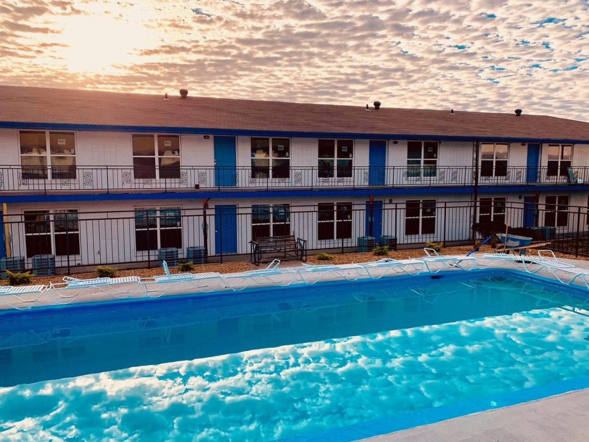 Motel with blue trim and pool in front. Cloudy sky.