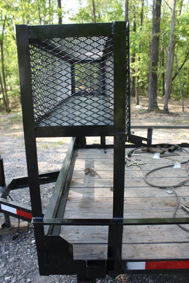 A trailer with a cage on top of it is parked in the woods.