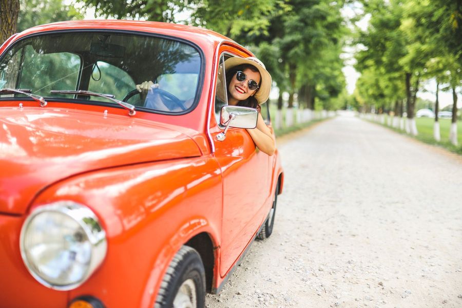 A woman is peeking out of the window of a red car.