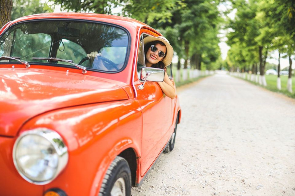 A woman is peeking out of the window of a red car.