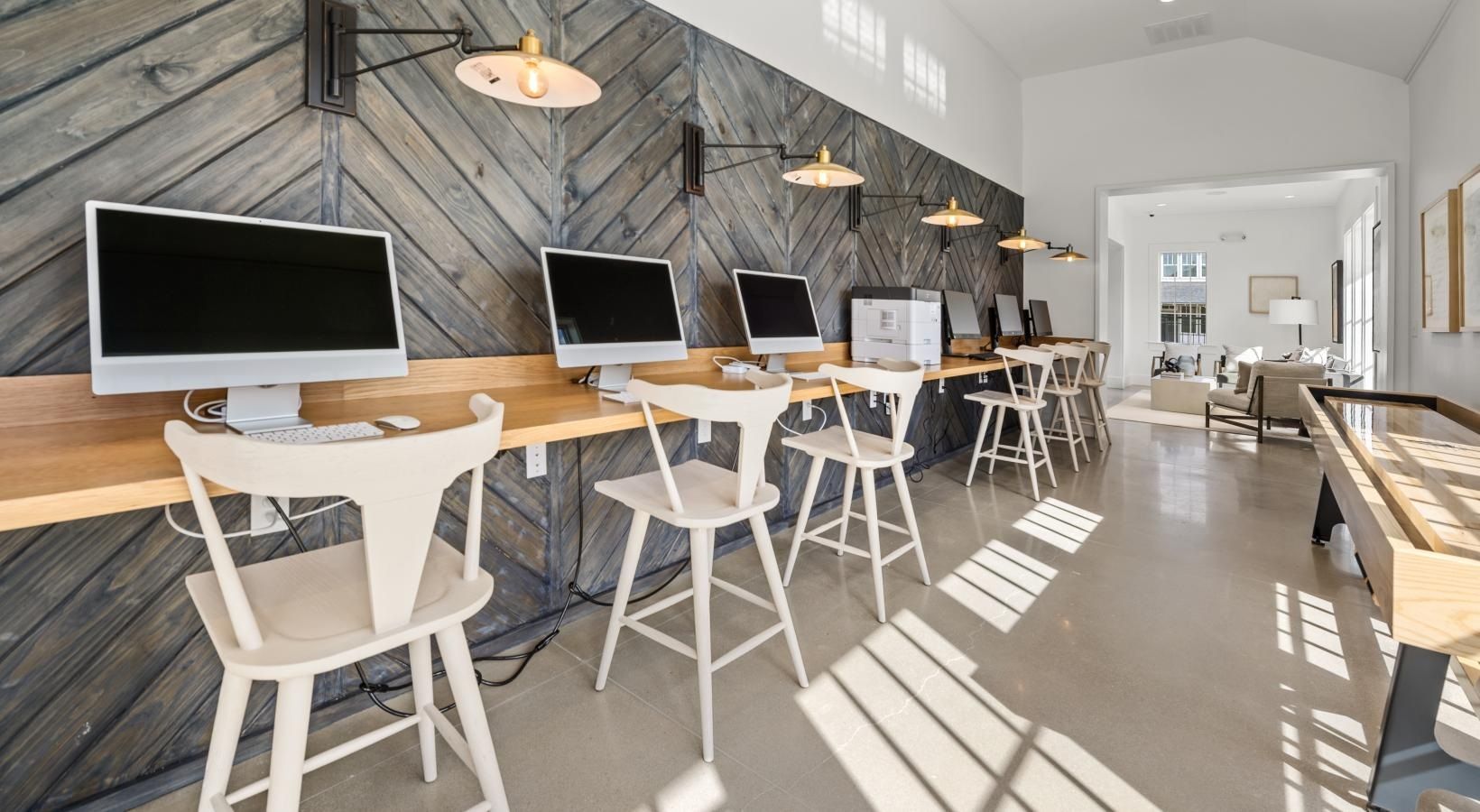 Row of computer stations with white chairs along a wooden counter in a modern community room.