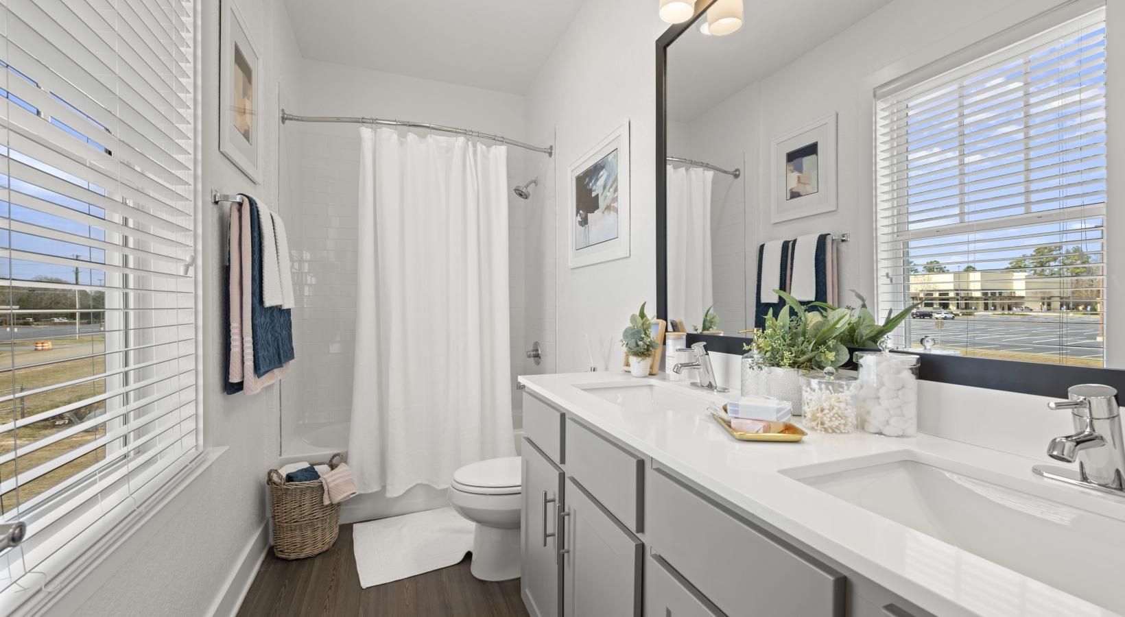 Bright bathroom with double-sink vanity, white countertops, and a window with horizontal blinds.