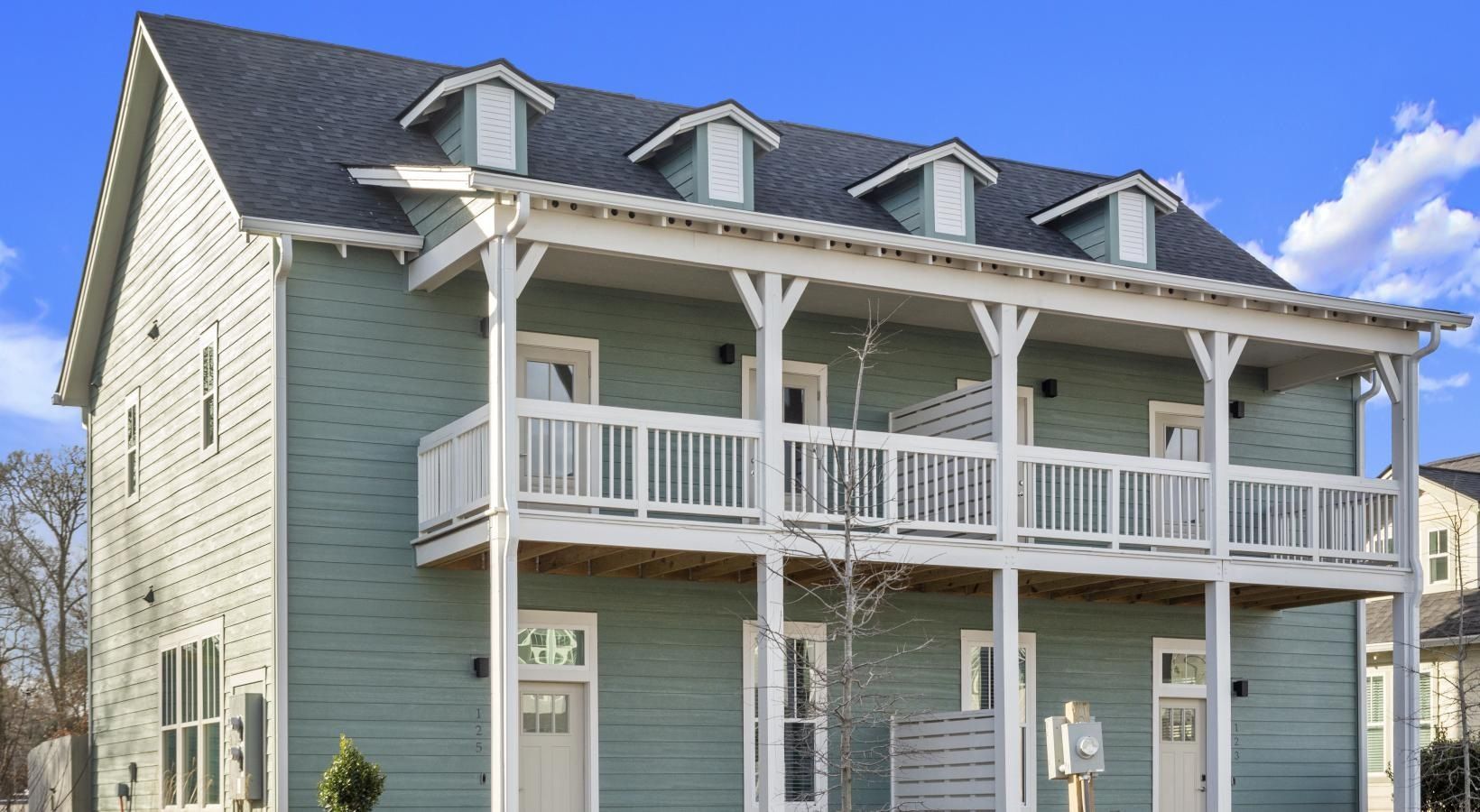 Exterior view of a light-blue, two-story apartment building with a white wraparound balcony.