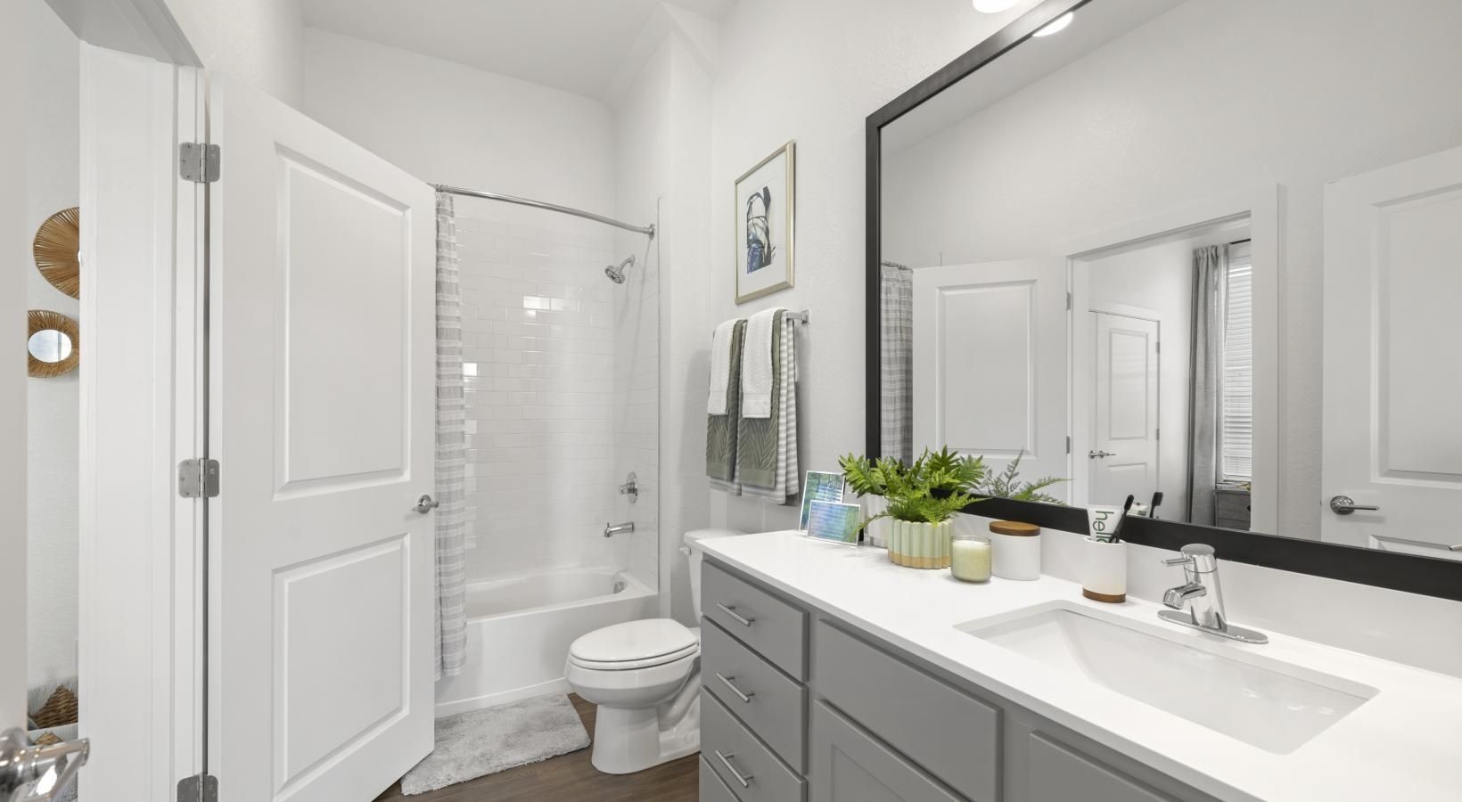 Modern apartment bathroom with white vanity, large mirror, tub/shower, and towels.