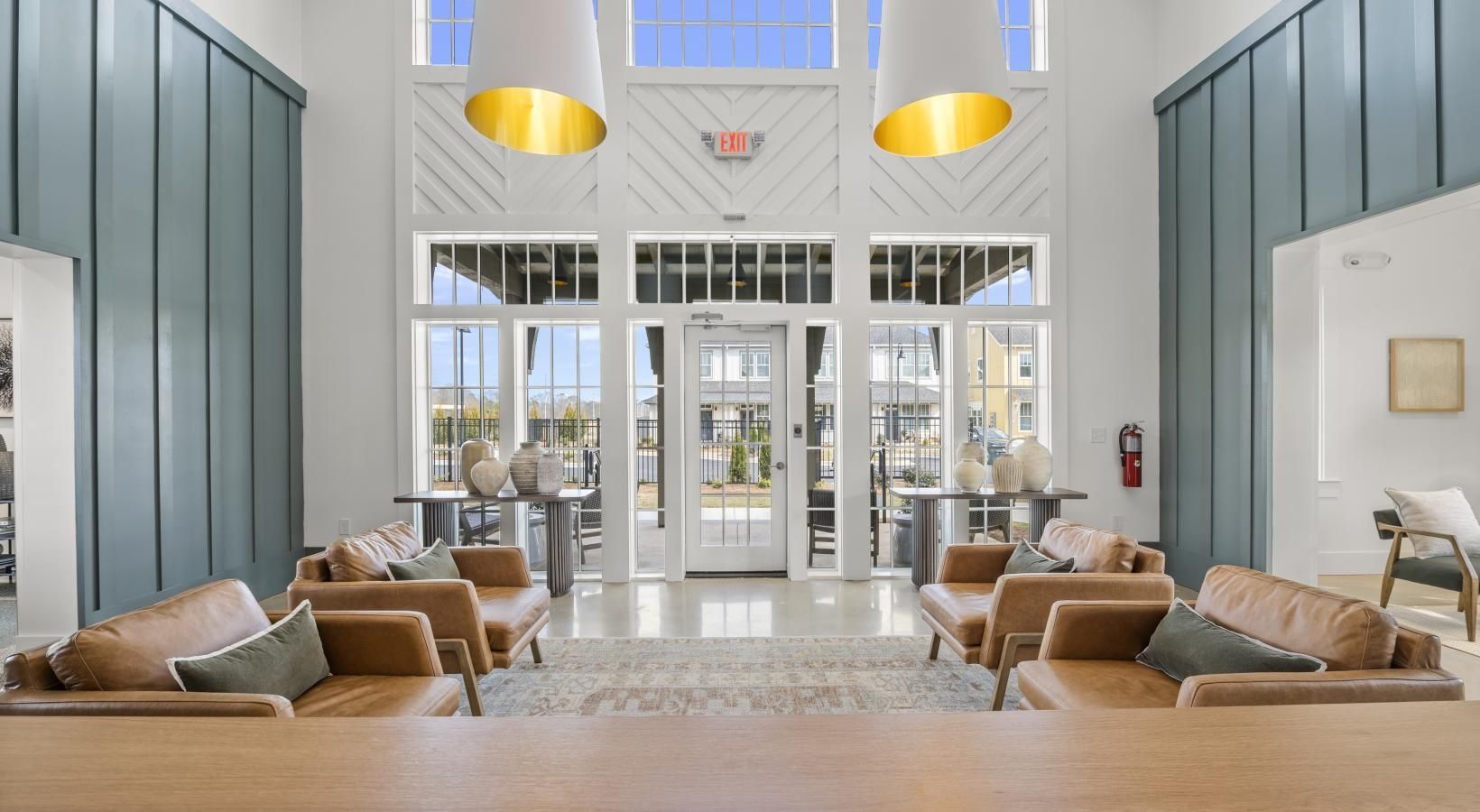 Modern residential lobby with teal accent walls, leather seating, and tall glass entry doors.
