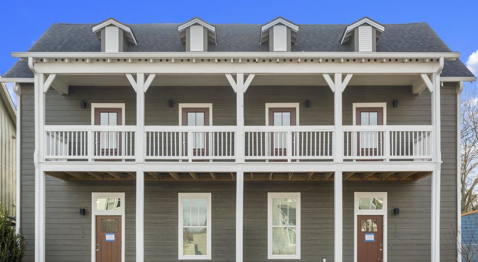 Two-story apartment building exterior with a wraparound balcony and multiple ground-floor doors.