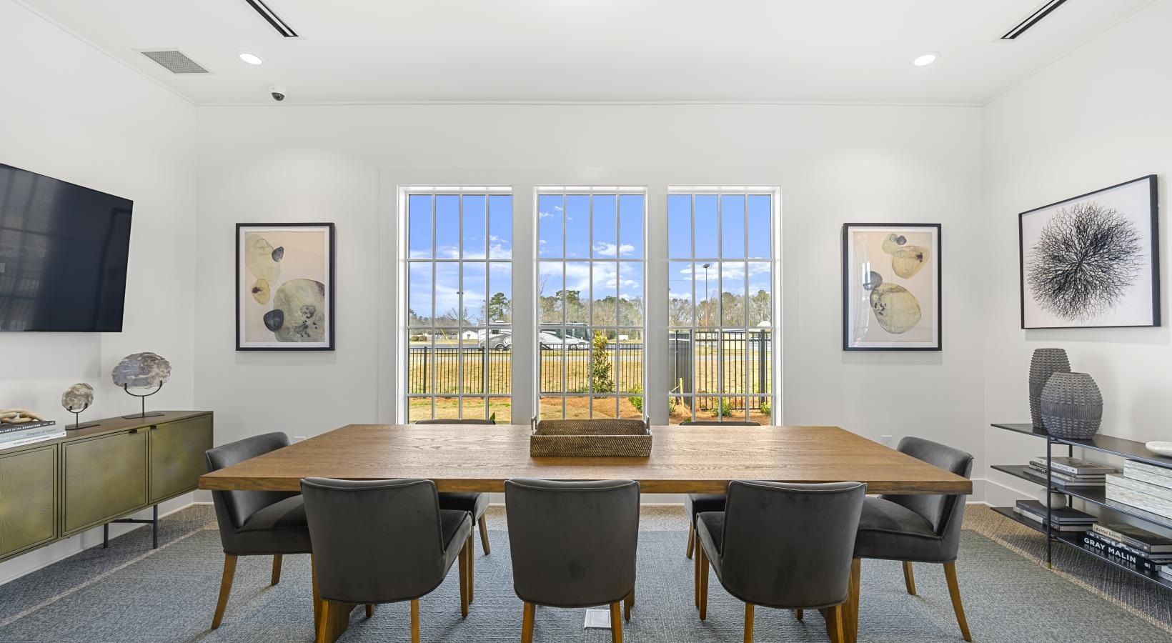 Bright conference room with a long wooden table, six dark chairs, and large windows.