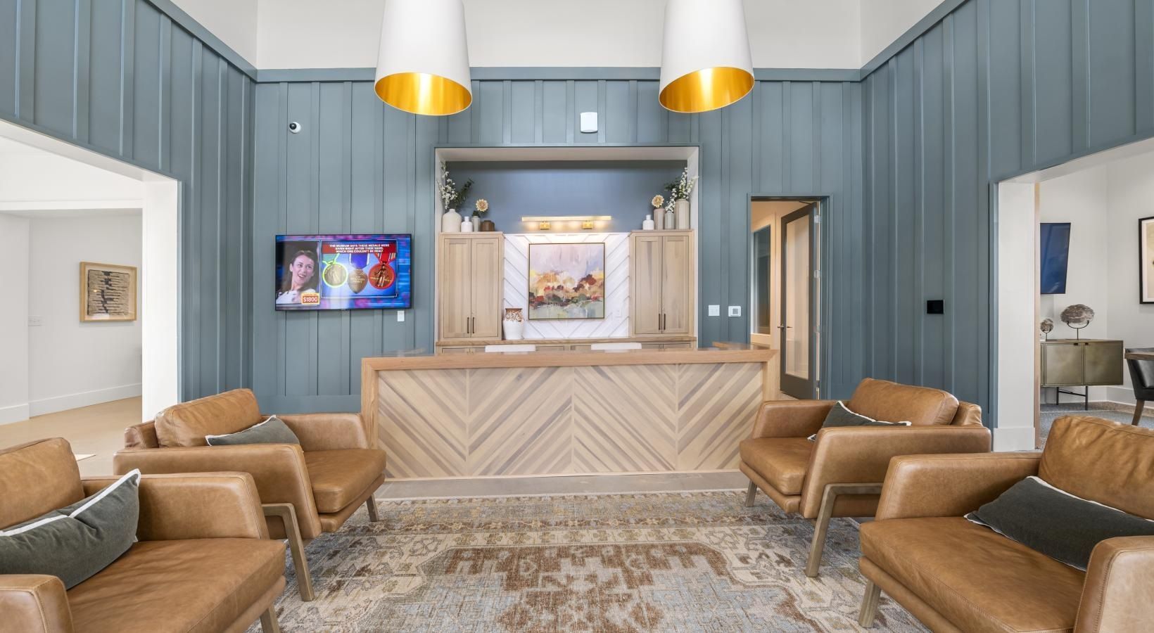 Apartment community lobby with blue paneled walls, a wooden front desk, and brown leather seating.