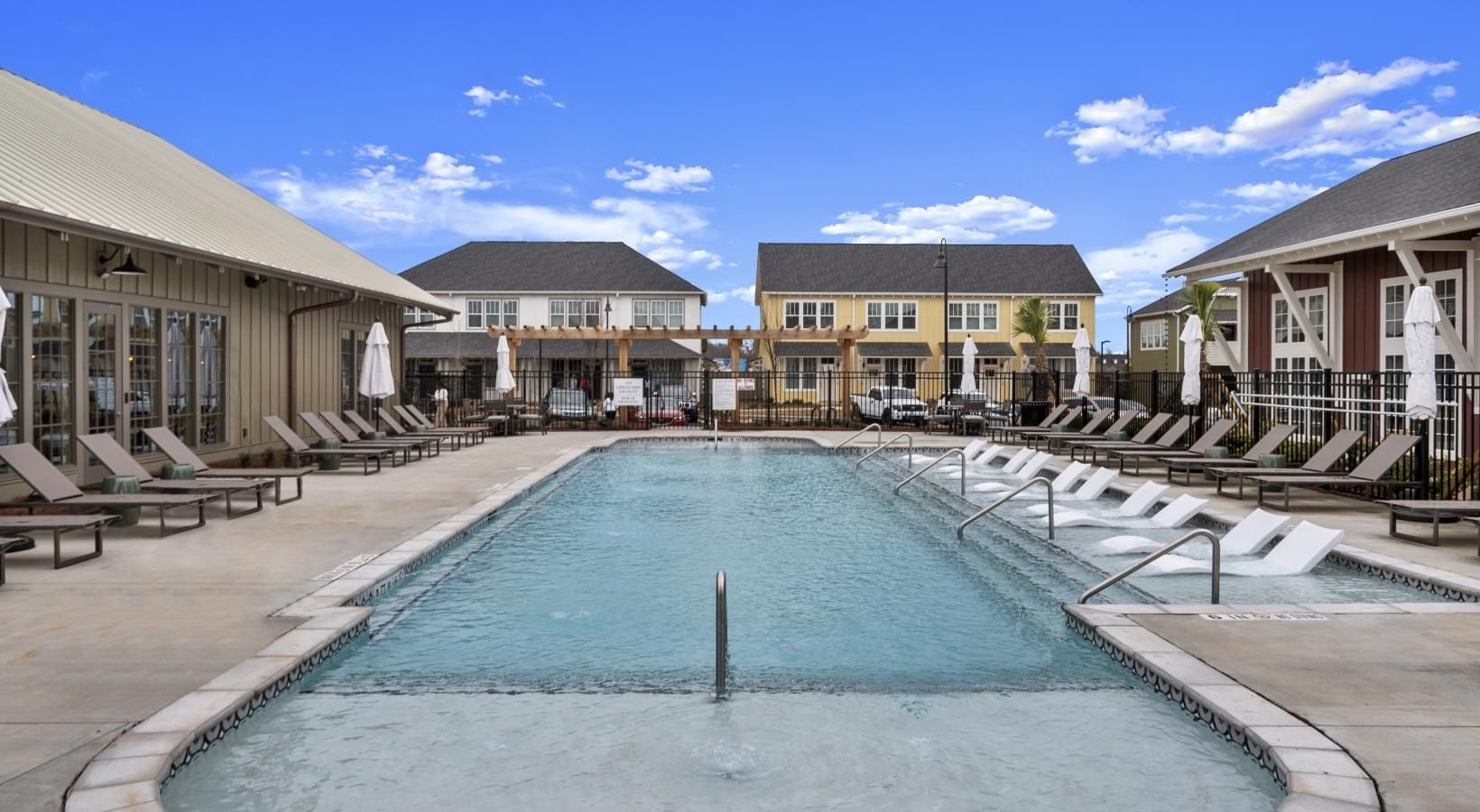 Outdoor community pool area with lounge chairs and umbrellas.