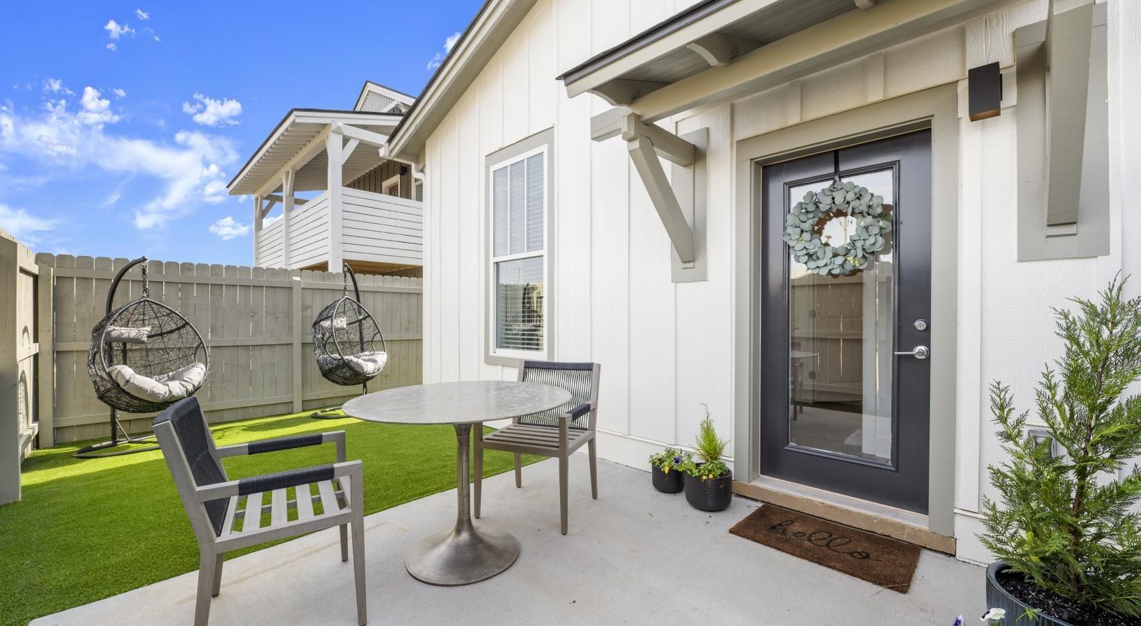 Patio area beside an apartment door with a round table, two chairs, and hanging egg chairs.