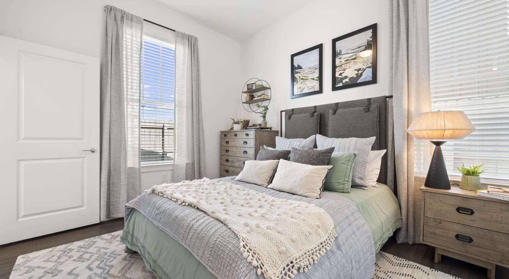 Bright bedroom in a furnished apartment with a bed, dresser, and large windows