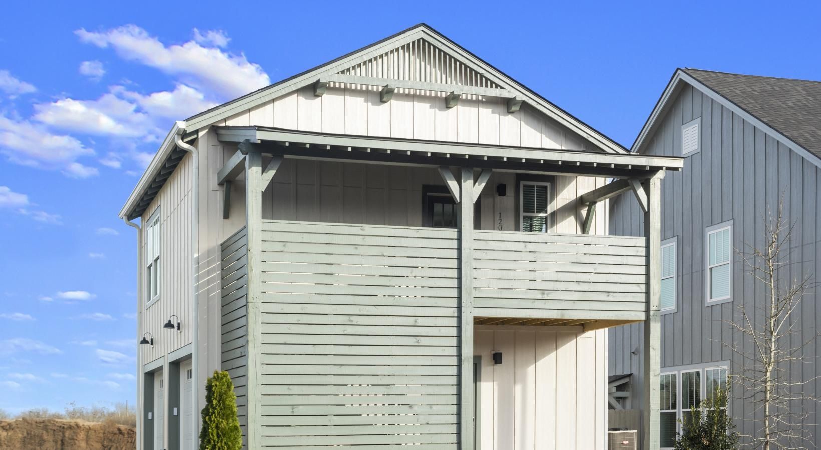 Exterior view of a light gray townhouse-style apartment with a balcony under a blue sky.
