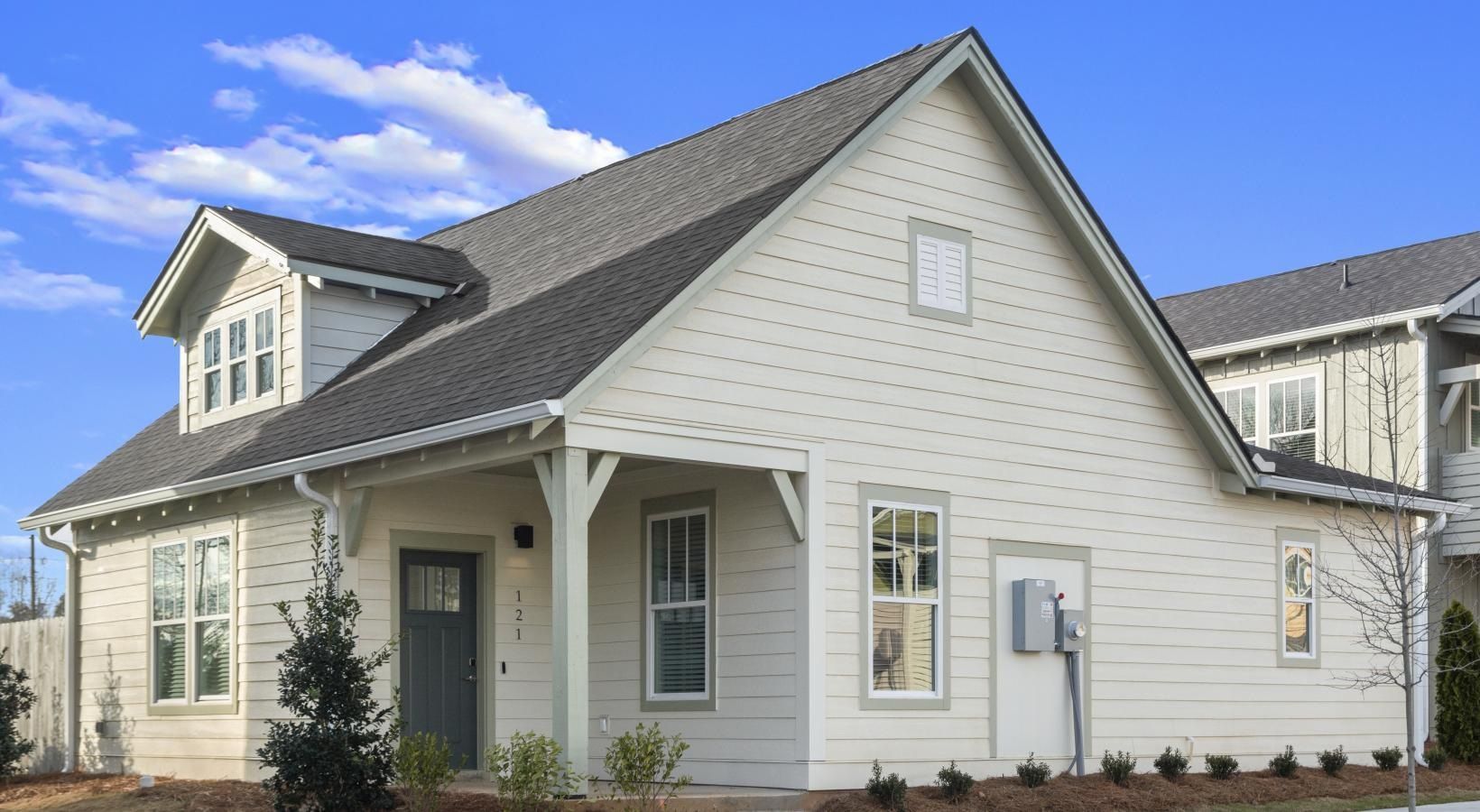 Exterior view of a beige townhome with a gabled roof and front porch.