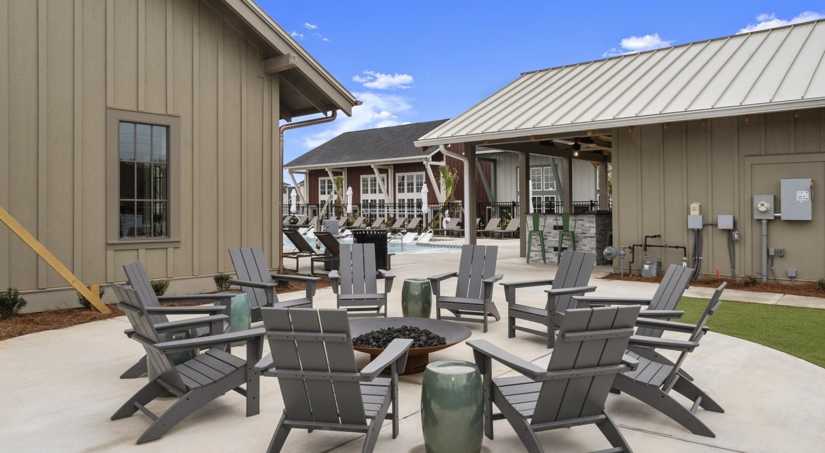 Outdoor community lounge with a circular arrangement of chairs around a fire pit, pool in the background.