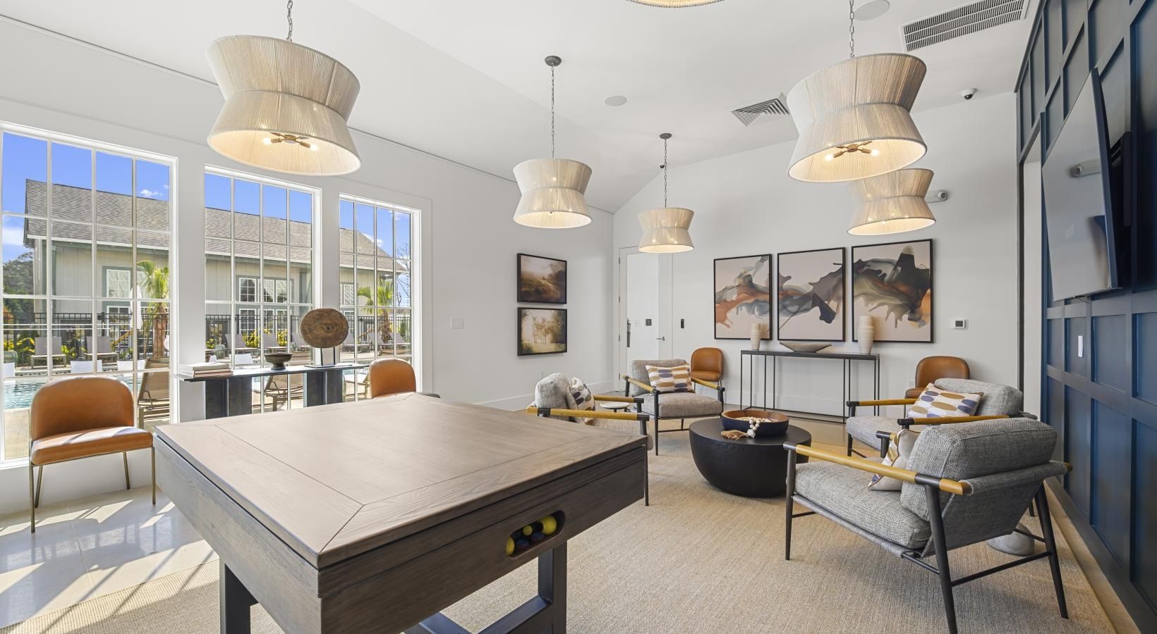 Bright clubhouse lounge with a pool table, sofas, and large windows overlooking the pool.