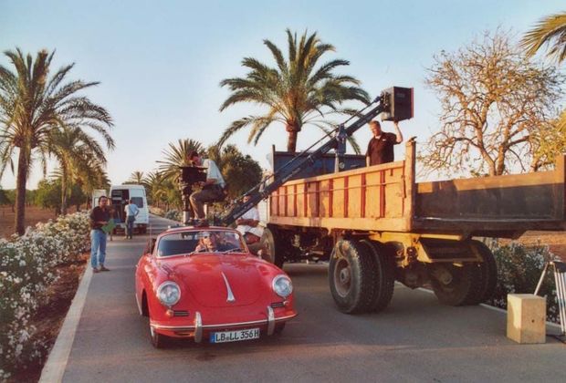 Roter Oldtimer Porsche auf Landstraße mit Palmen auf Mallorca. Werbefilmteam mit großer Kamera auf einem LKW-Kran filmt die Szene. 