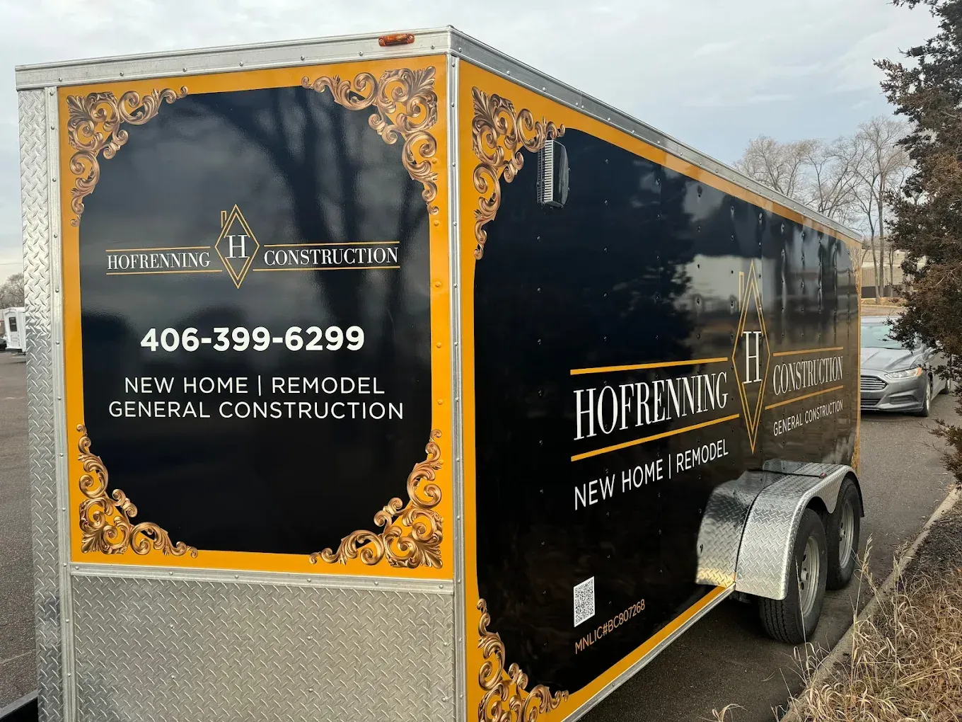 Black construction trailer with gold trim and logo for Hofrenning II Construction; 406-399-6299.