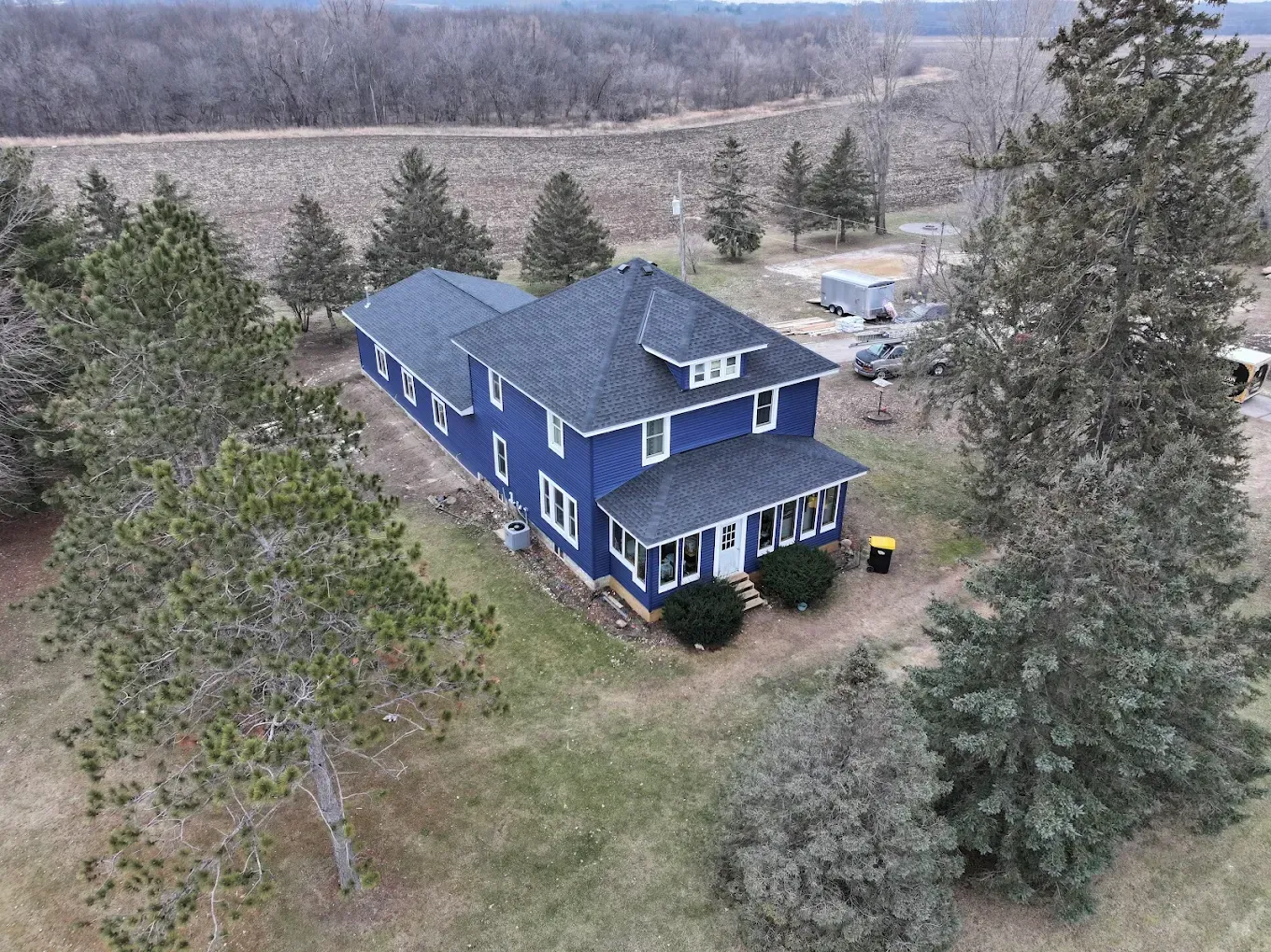 Blue two-story house with dark roof and white trim surrounded by trees in a rural setting.