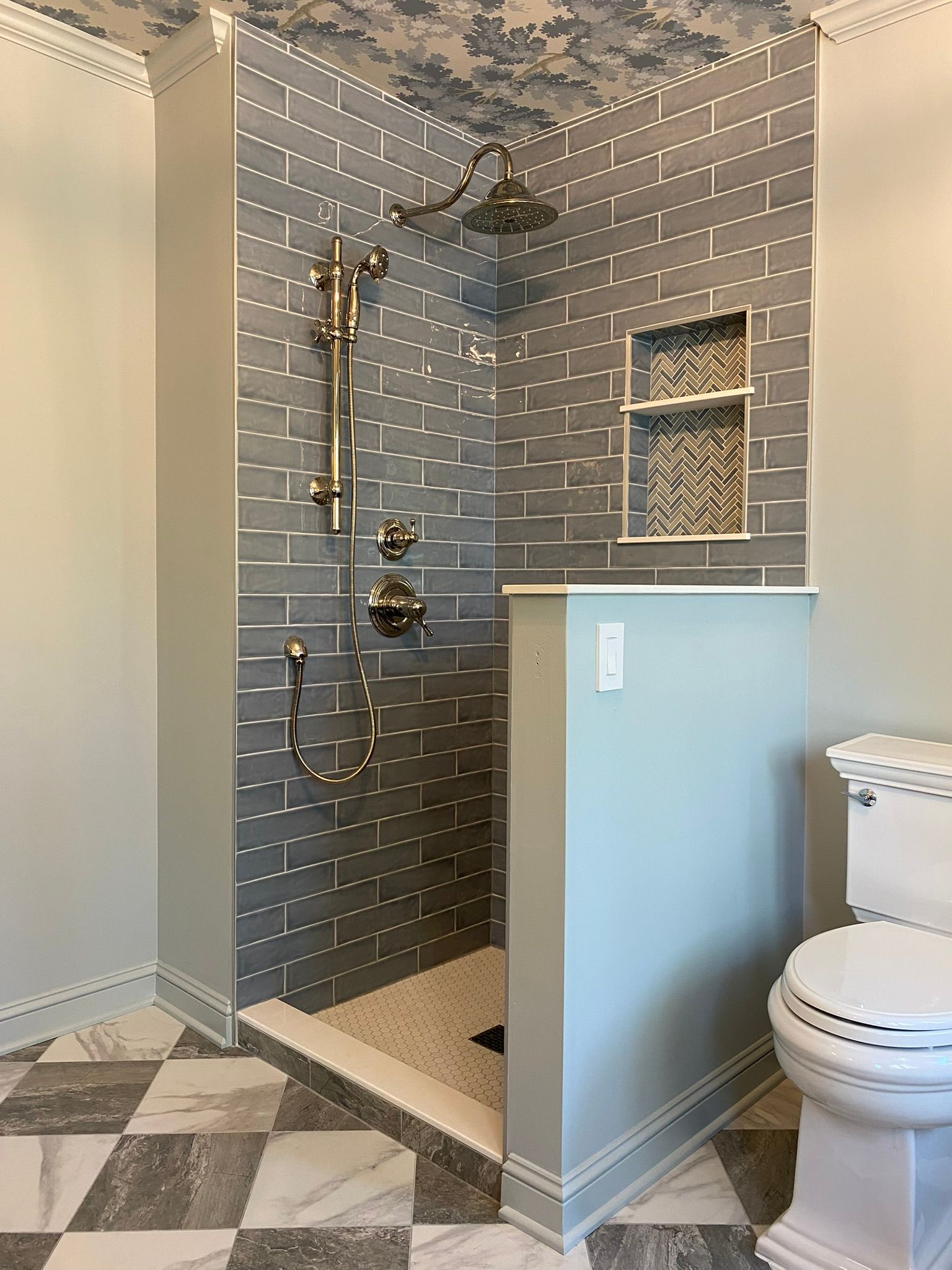 Bathroom with gray tiled shower, light blue walls, and patterned tile floor.